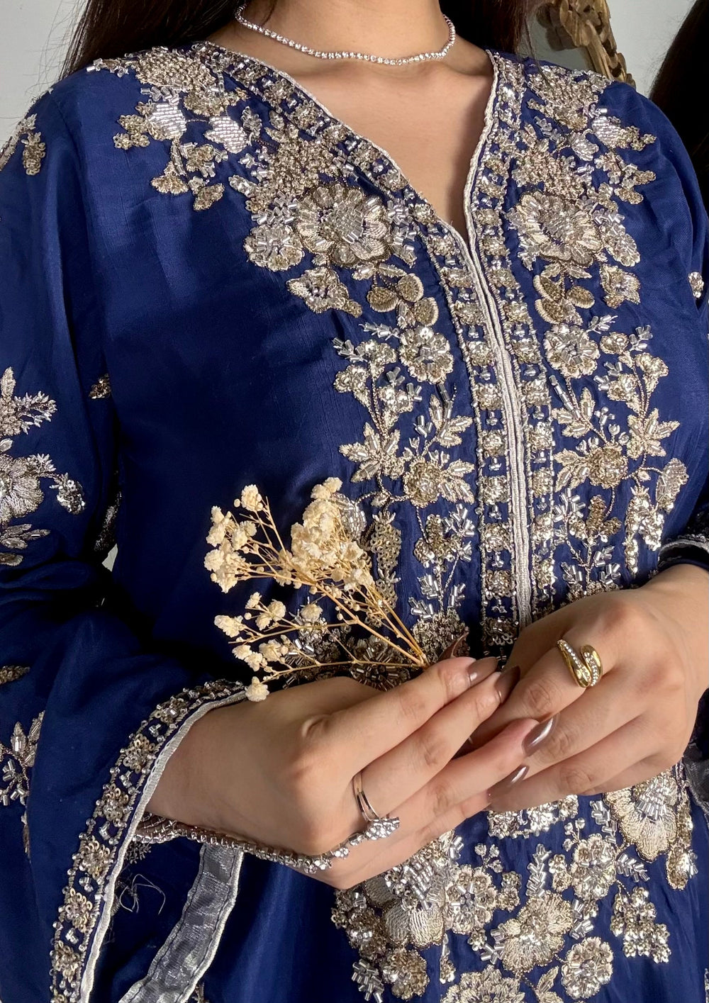 Macro shot of intricate gold and silver tilla handwork, sequins, and kora dabka detailing around the V-neckline of a royal blue luxury pret shirt.