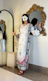 A woman models a long white embroidered dress with blue and pink borders, standing in front of a large ornate gold mirror in an indoor setting.