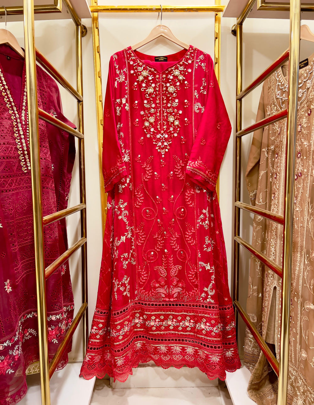 Red embroidered gown dress on a hanger with gold racks and other dresses in the background