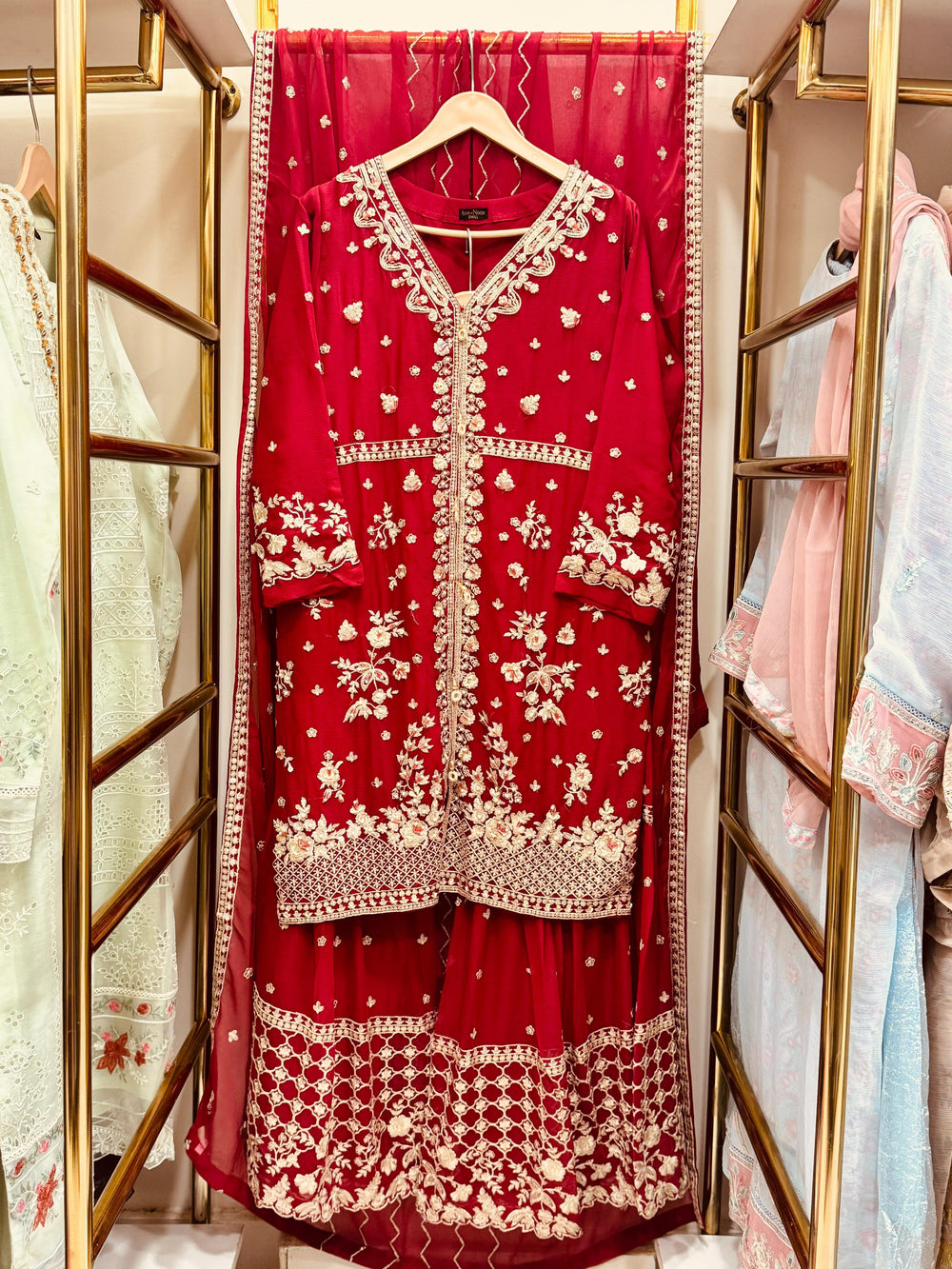 Red embroidered traditional outfit on a hanger with a gold frame.