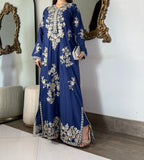 Angled shot of a model wearing an elegant royal blue embroidered maxi gown holding a silver clutch, emphasizing the rich drape of raw silk.