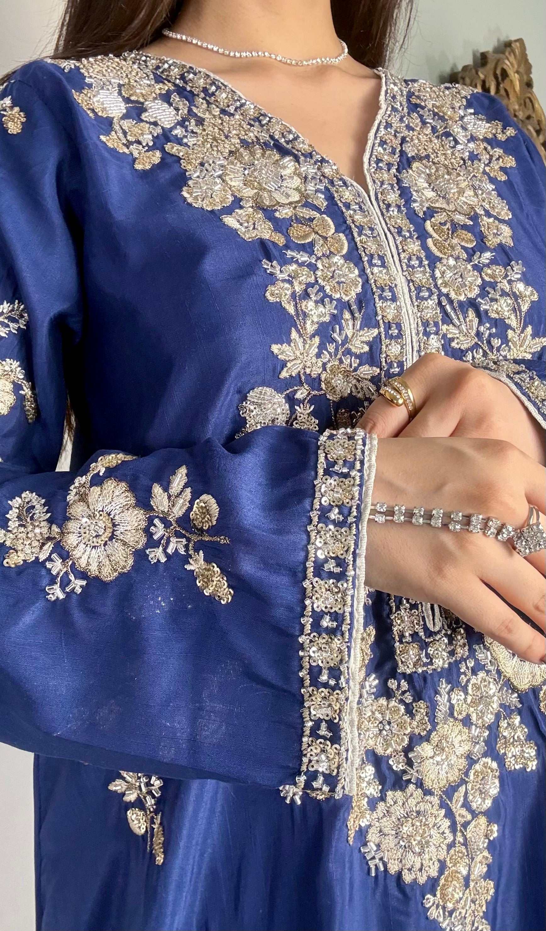 Close-up details of silver floral hand-embroidery and tilla work on the sleeve cuff and bodice of a royal blue raw silk festive dress.