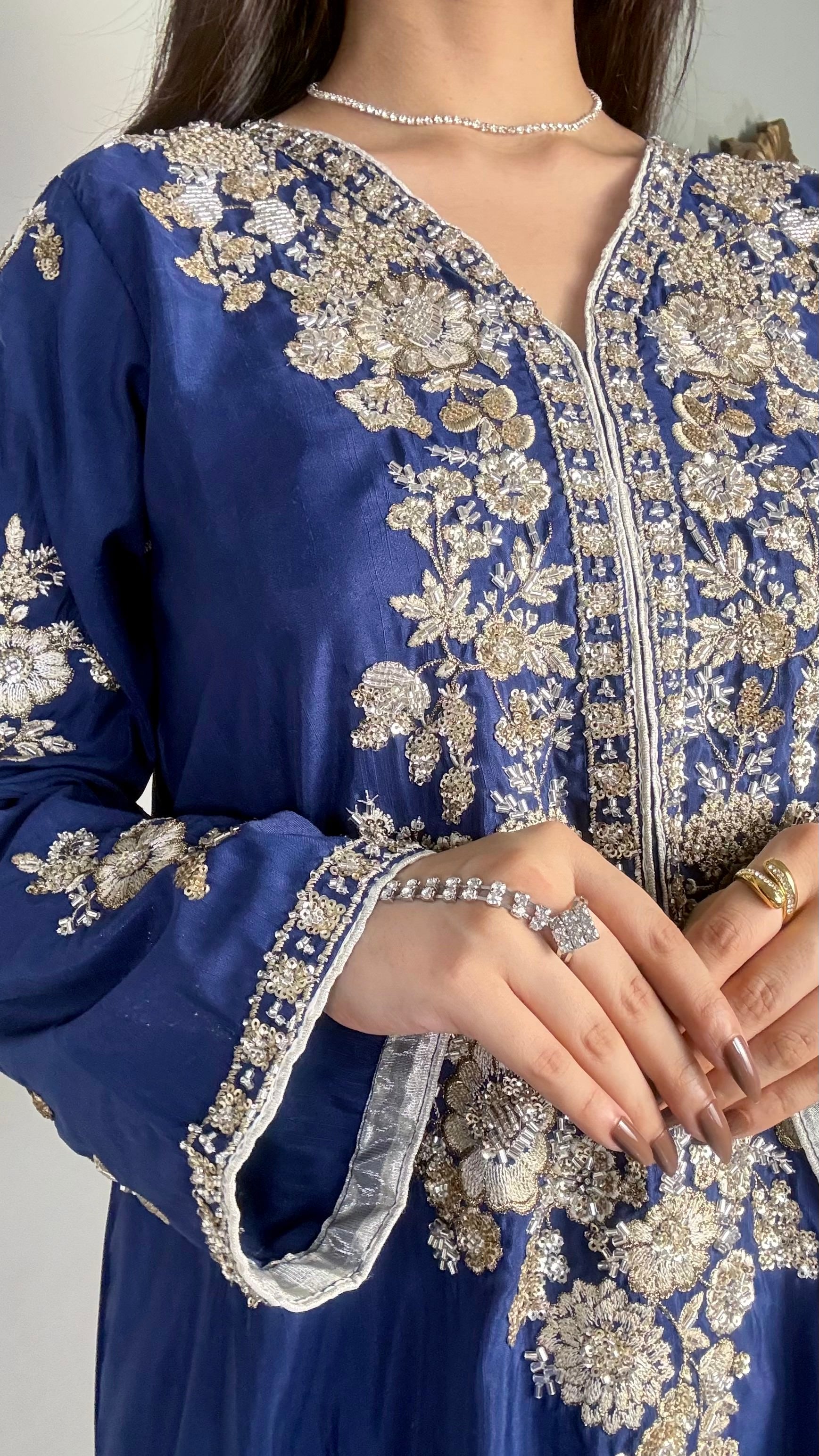 Detailed close-up of a model's hands over the heavily worked V-neck bodice of a royal blue pakistani festive wear outfit.