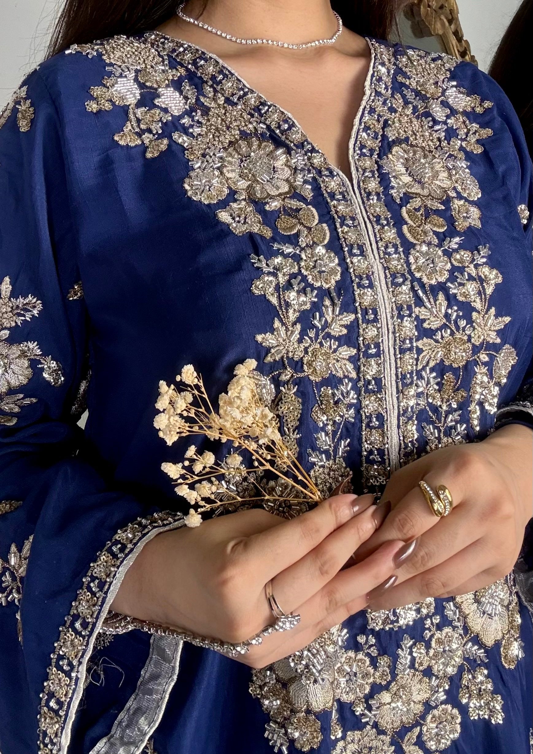 Macro shot of intricate gold and silver tilla handwork, sequins, and kora dabka detailing around the V-neckline of a royal blue luxury pret shirt.