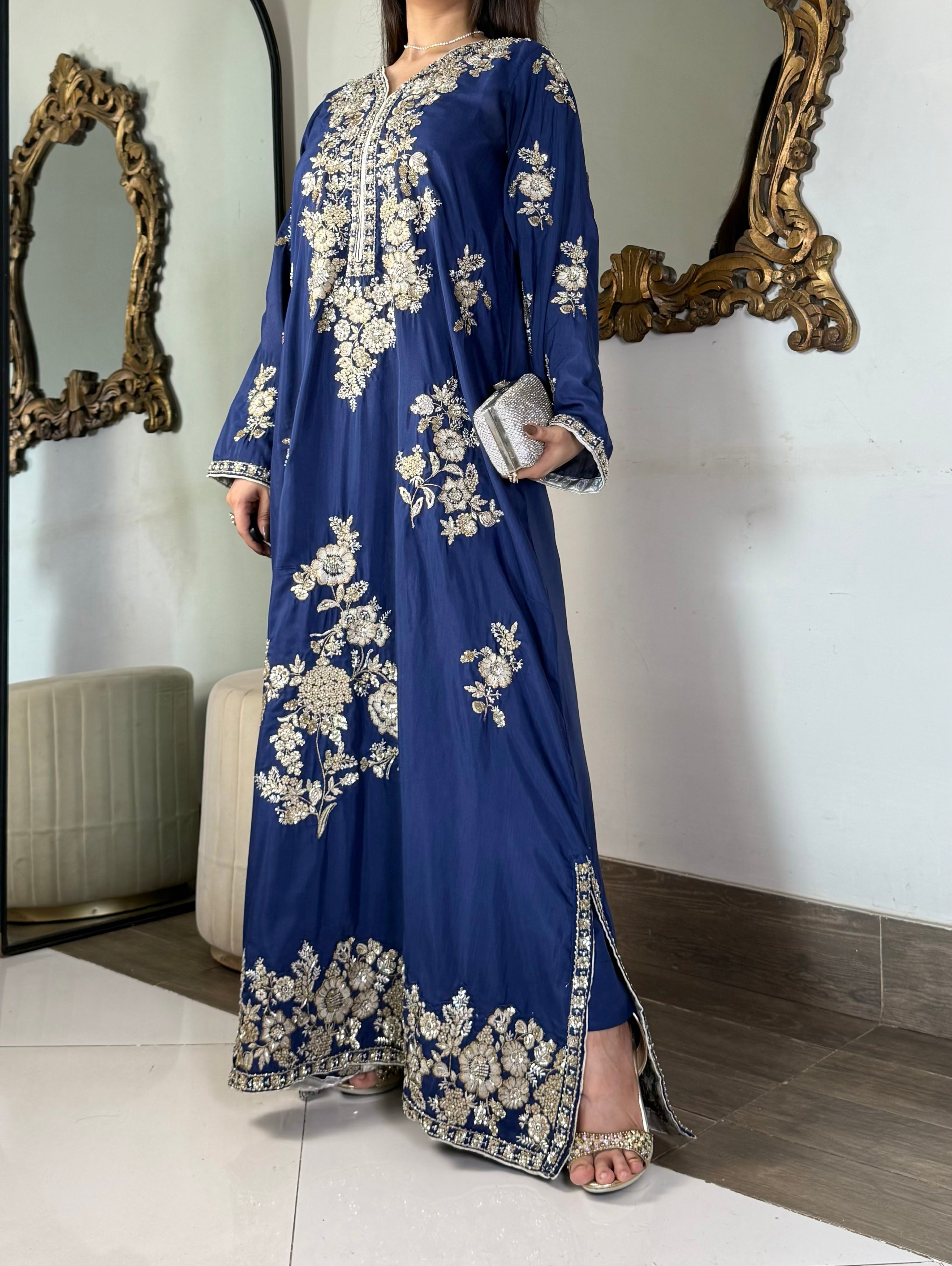 Side profile of a model wearing a luxurious royal blue embroidered raw silk kaftan gown, highlighting the flowing silhouette and tailored fit.