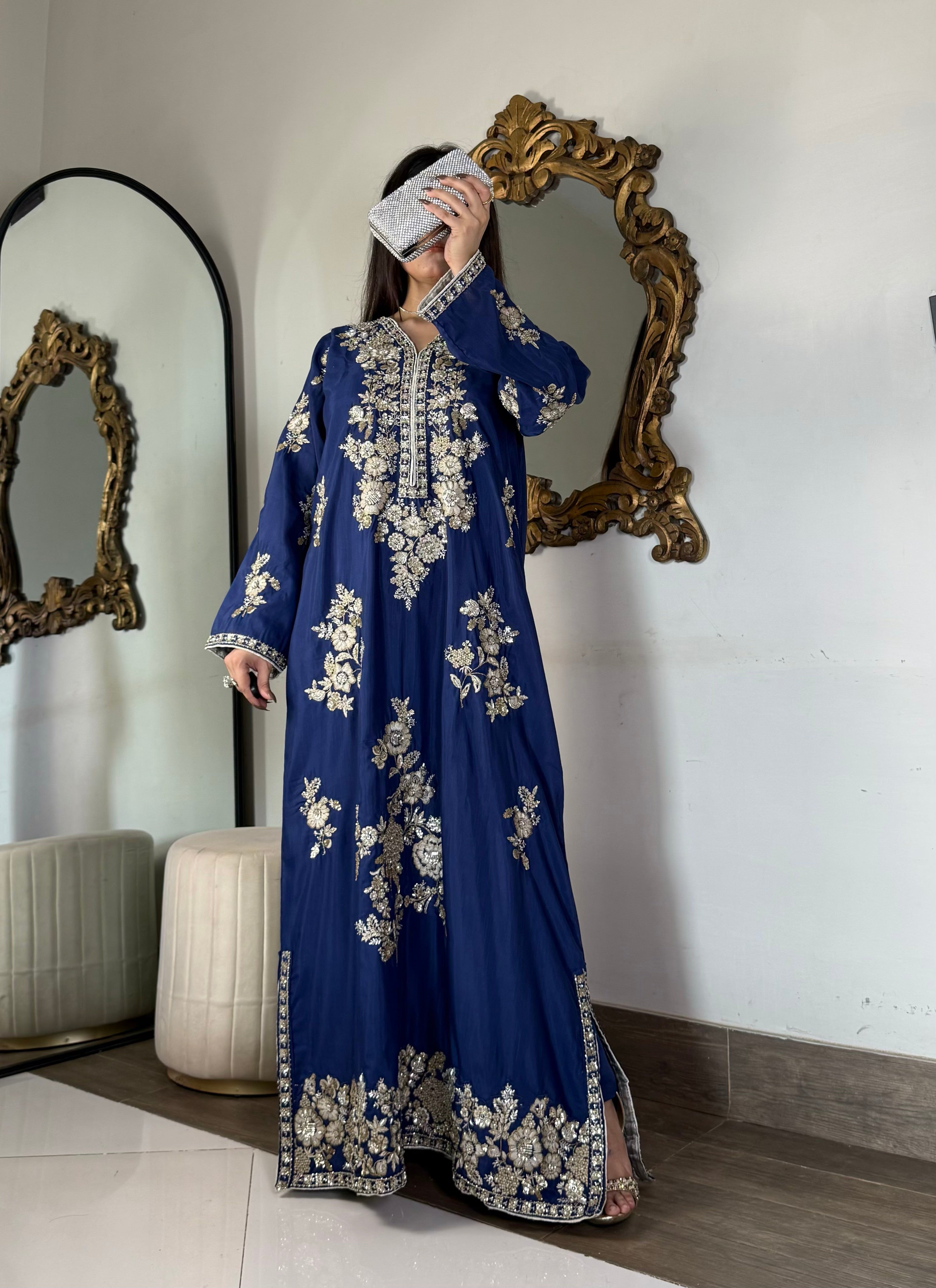 Full-length view of a model showcasing a stitched royal blue raw silk maxi dress with high side slits and a silver-embellished metallic clutch.